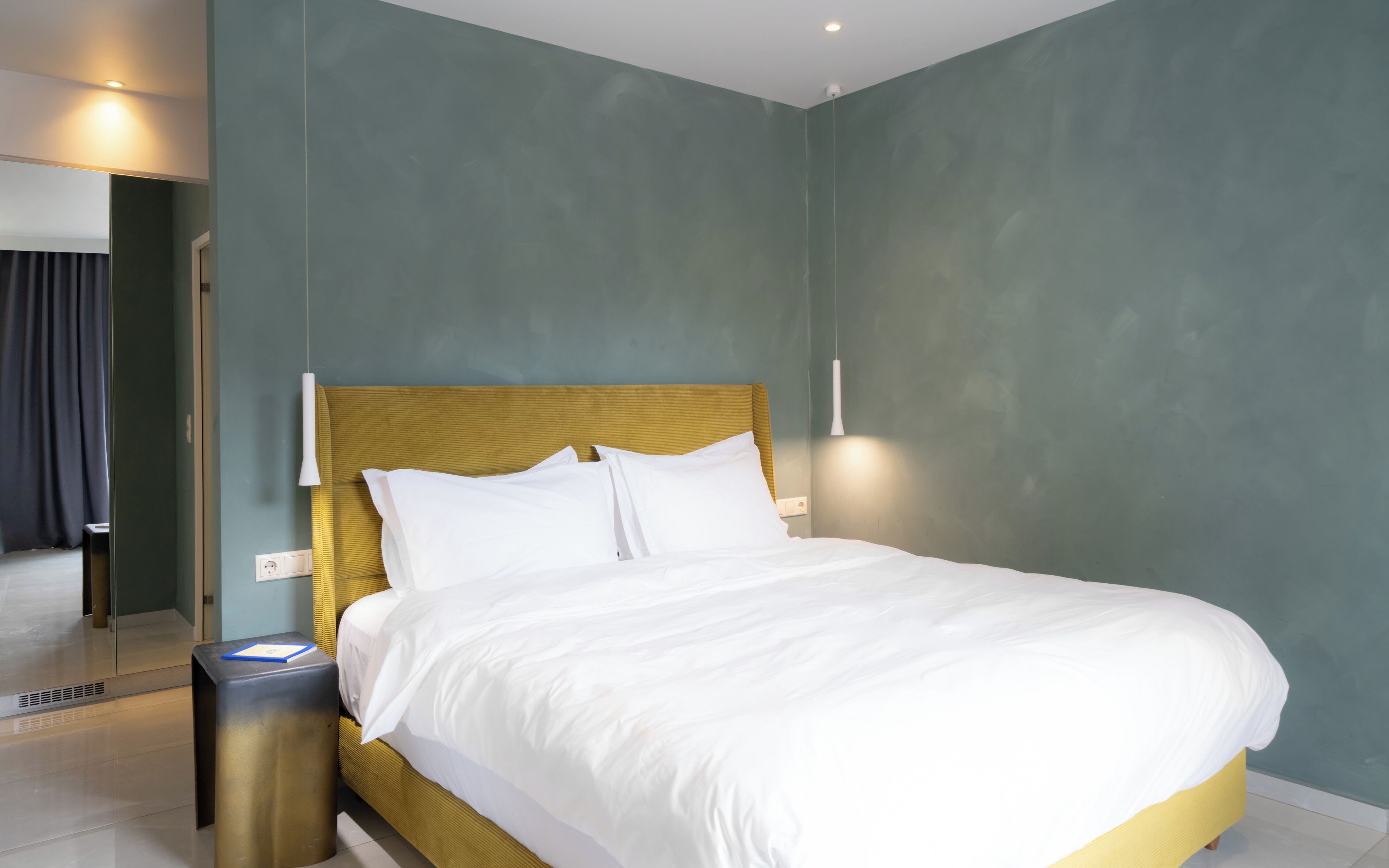 A neatly made bed with white linens, a gold headboard, and a bedside table with a lamp.