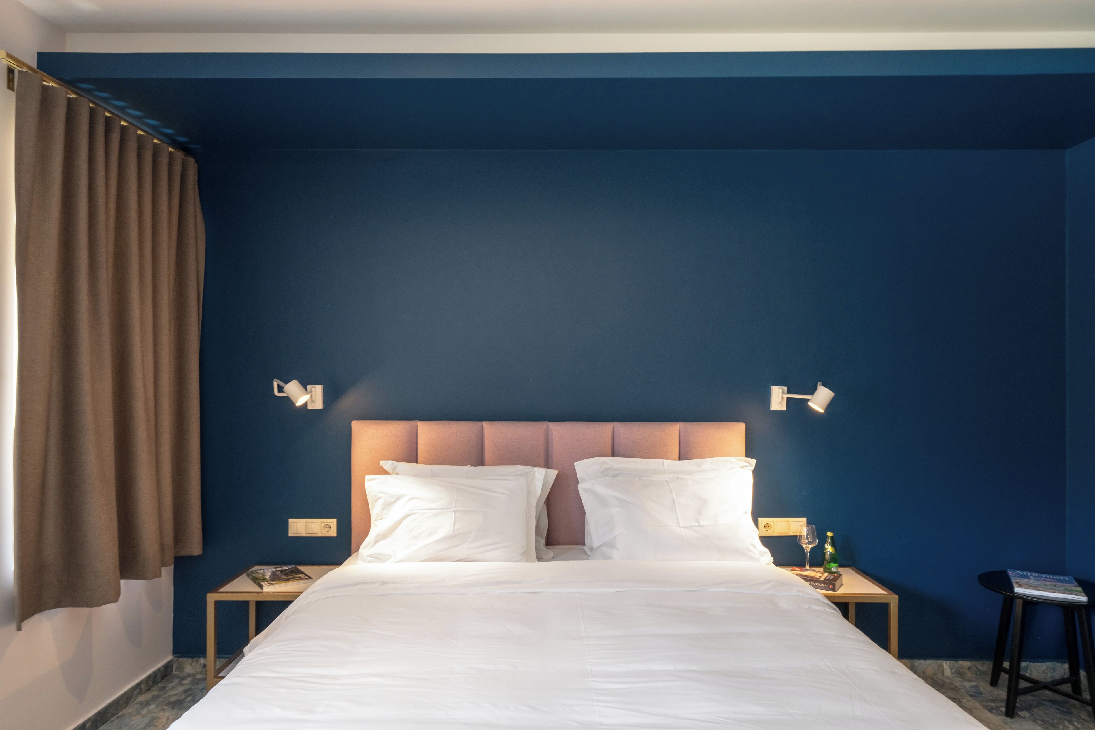 Una habitación de hotel con una cama grande, dos mesitas de noche, una lámpara y una ventana con cortinas.