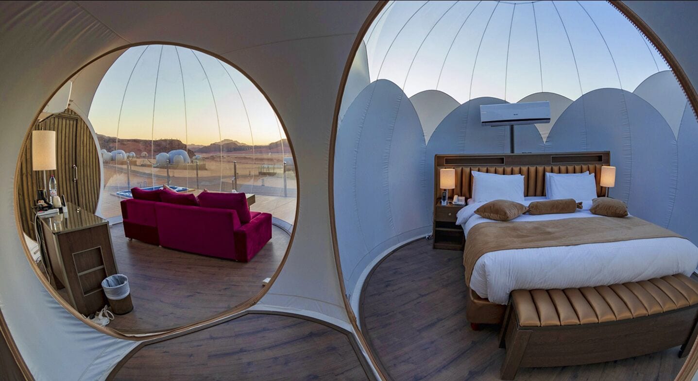 A modern, circular room with a bed, a seating area, and a view of the landscape.