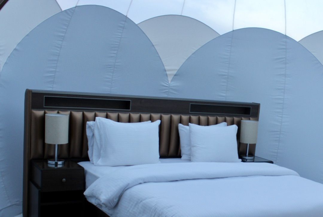A modern hotel room with a large bed, two bedside tables with lamps, and a unique ceiling design.