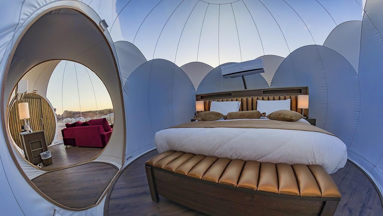 A dome-shaped room with a bed, a bench, a circular window, and a red chair.