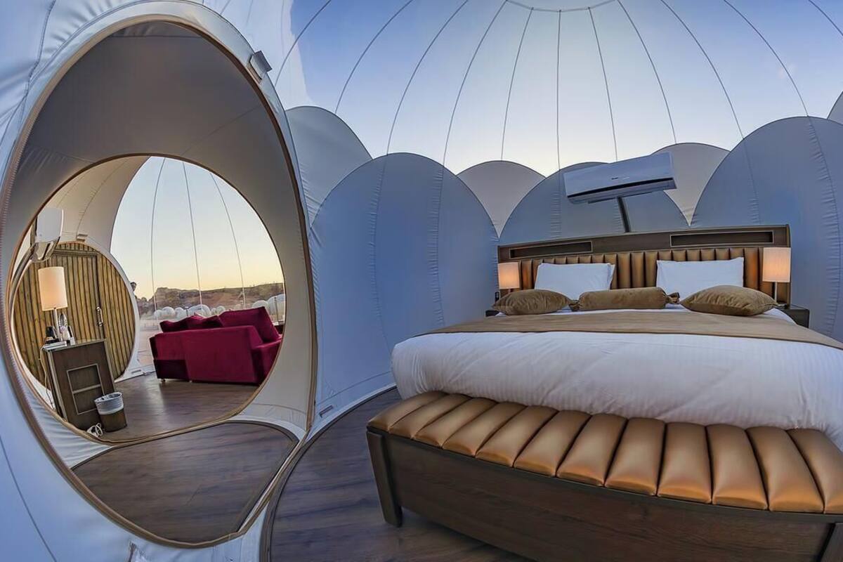 Une pièce en forme de dôme, comprenant un lit, un banc, une fenêtre circulaire et une chaise rouge.