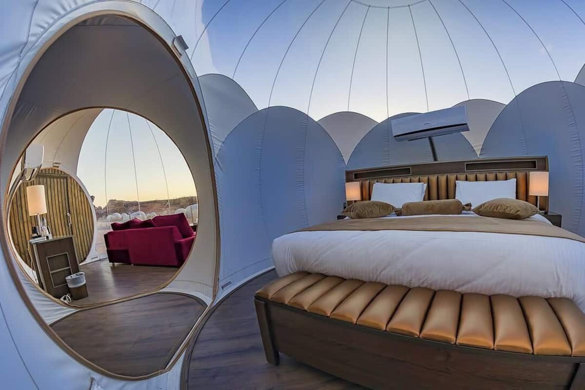 A dome-shaped room with a bed, a bench, a circular window, and a red chair.