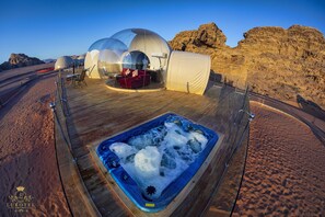 Un complexe hôtelier de luxe situé dans le désert, proposant des hébergements sous des dômes transparents, une terrasse en bois et un jacuzzi.