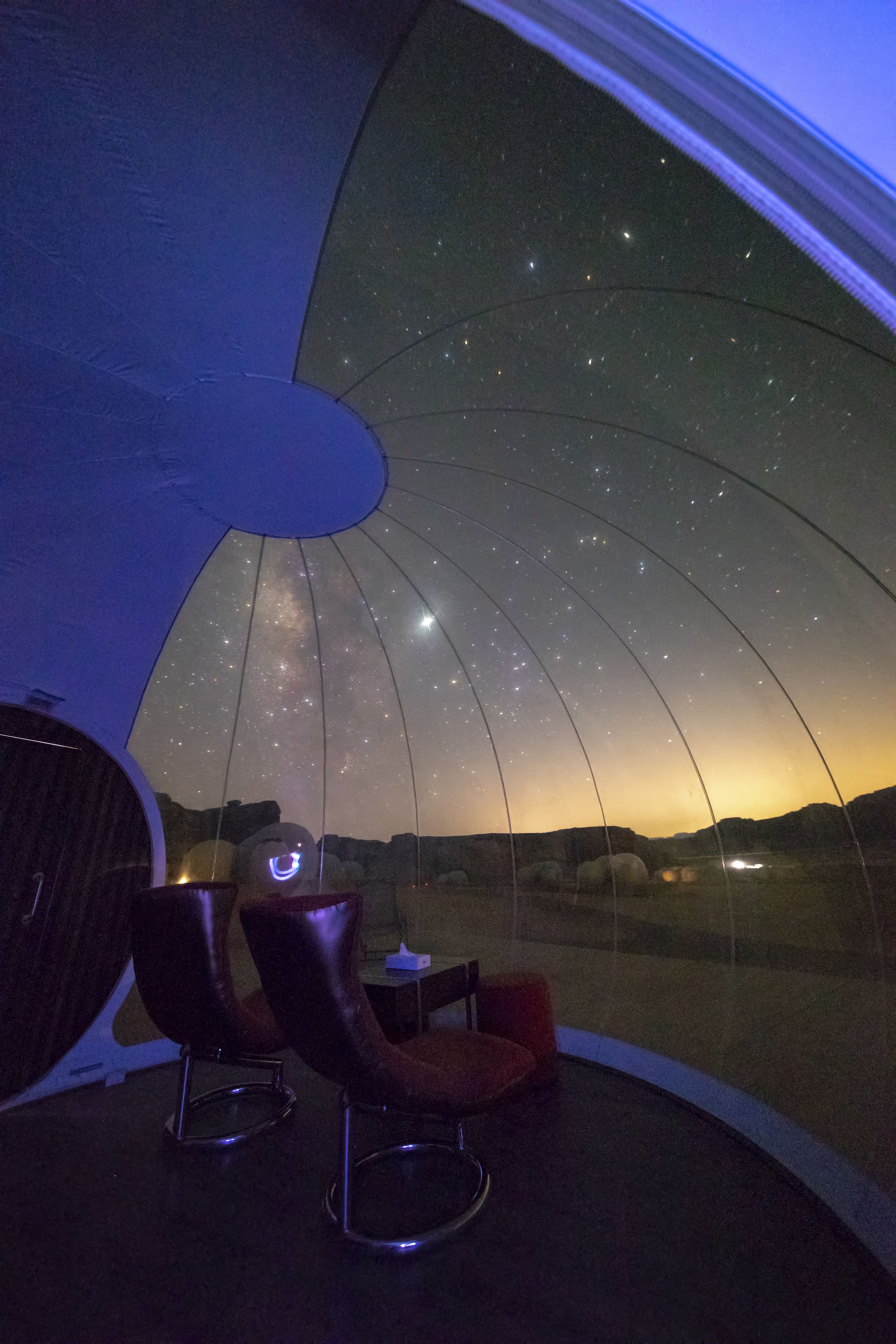 Un observatoire en forme de dôme offrant une vue dégagée sur le ciel nocturne. À l’intérieur, on trouve deux chaises et une petite table.