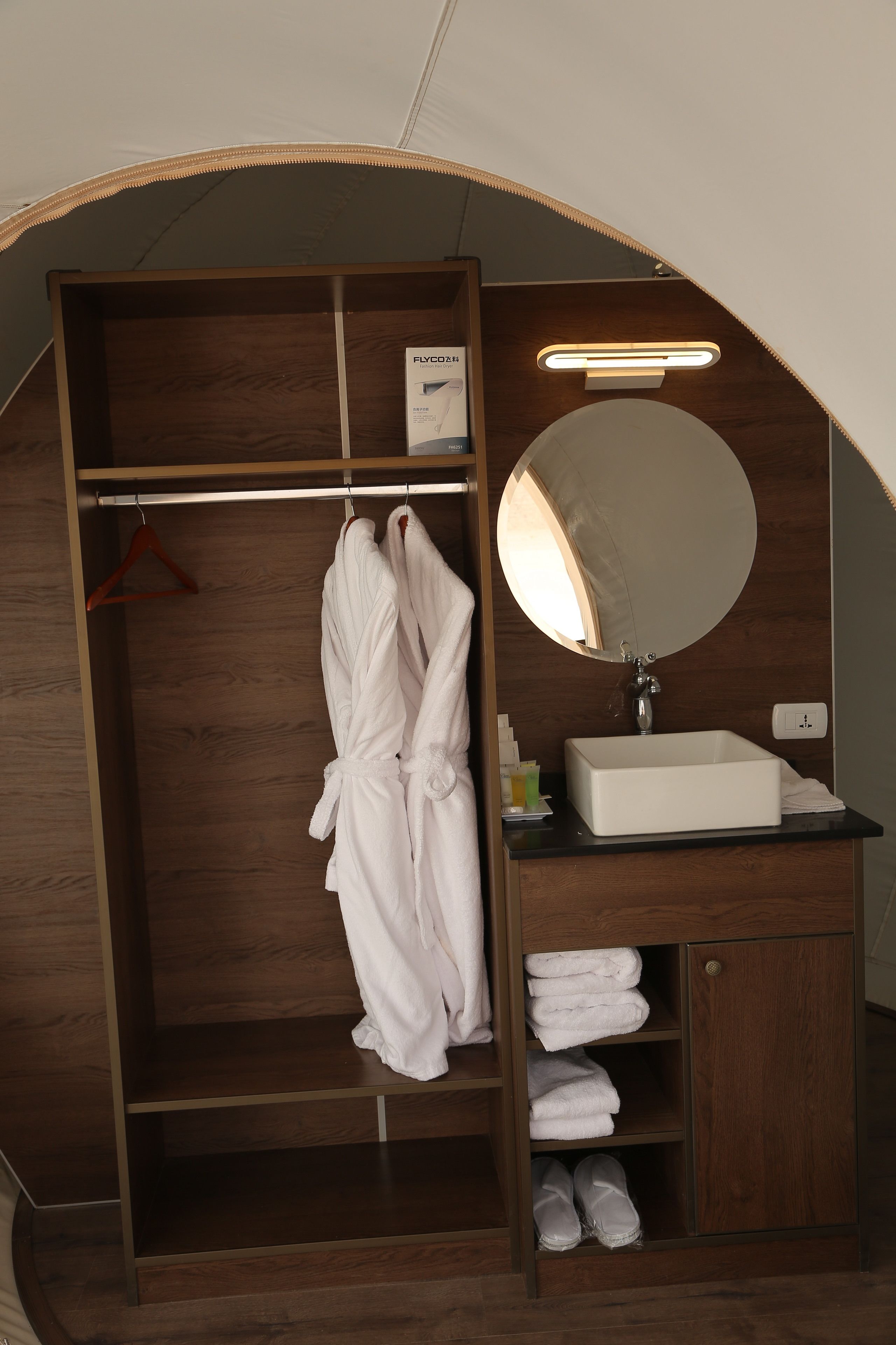 Een houten garderobe met een kledingroede, een spiegel en een wit wastafeltje.