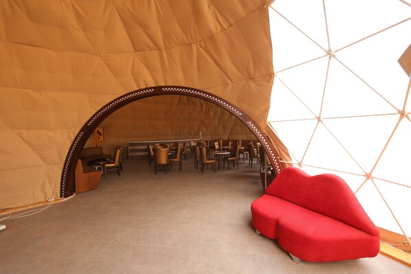 Une structure en forme de tente, à l’intérieur de laquelle on trouve un canapé rouge, ainsi que plusieurs tables et chaises.