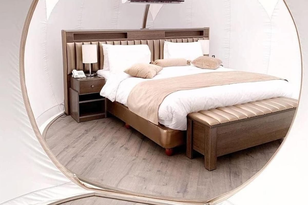 A circular room with a bed, bedside table, lamp, and an air conditioning unit.