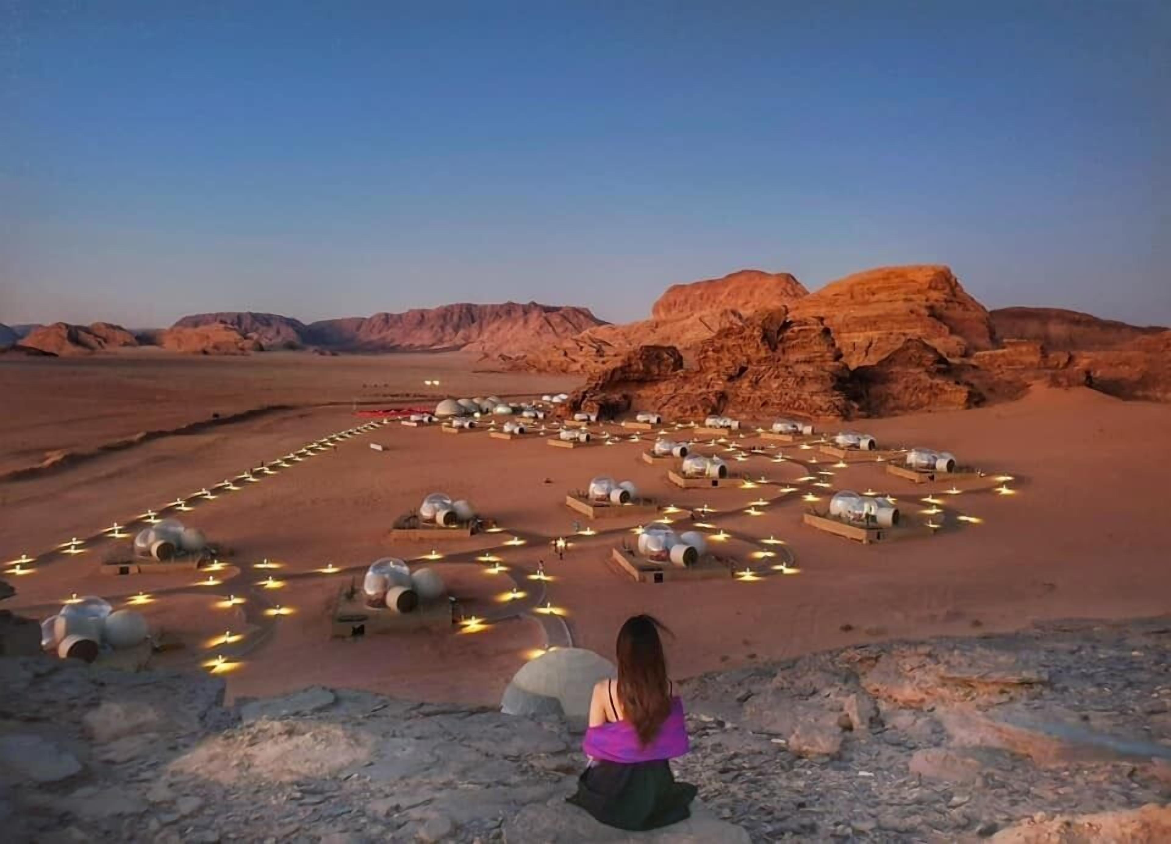 A desert landscape with spherical tents arranged in a circular pattern, illuminated by ground lights.