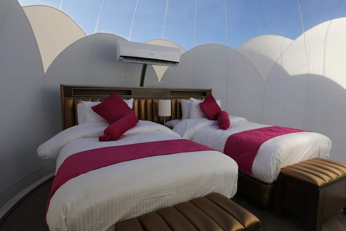 A hotel room with two beds, a ceiling fan, and a large window.