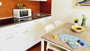 A compact kitchen with white cabinets, a microwave, and a sink. There is a dining table with chairs and a bowl of sunflowers. - Bright sea front apartment with balcony (Bibione)