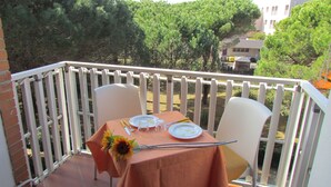 A balcony with a table set for two, chairs, and a view of trees and buildings. - Bright sea front apartment with balcony (Bibione)