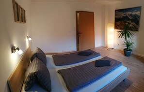 Een slaapkamer met twee eenpersoonsbedden, een houten hoofdbord, een kamerplant en een schilderij aan de muur.