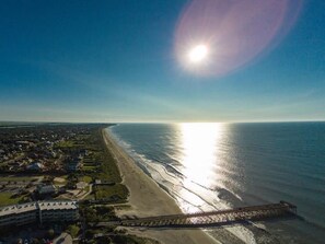 Vista aérea de una zona costera con playa, muelle y área residencial con casas y un hotel.