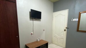 A room with a wooden door, a white wall-mounted TV, a white door, and a mirror on the right wall. - Stada Hotel (Kota Bharu)