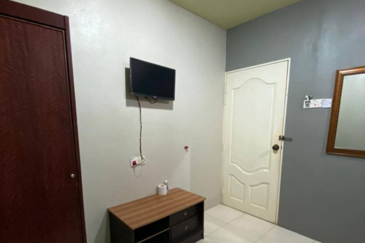 Una habitación con puerta de madera, televisor blanco montado en la pared, una puerta blanca y un espejo en la pared derecha.