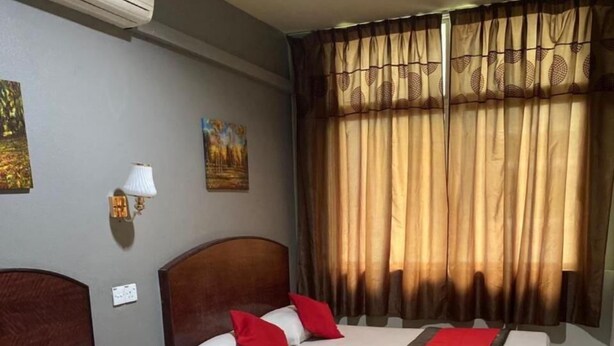 A hotel room with two beds, a wall-mounted air conditioner, a painting, a wall lamp, and a window with curtains. - Stada Hotel (Kota Bharu)