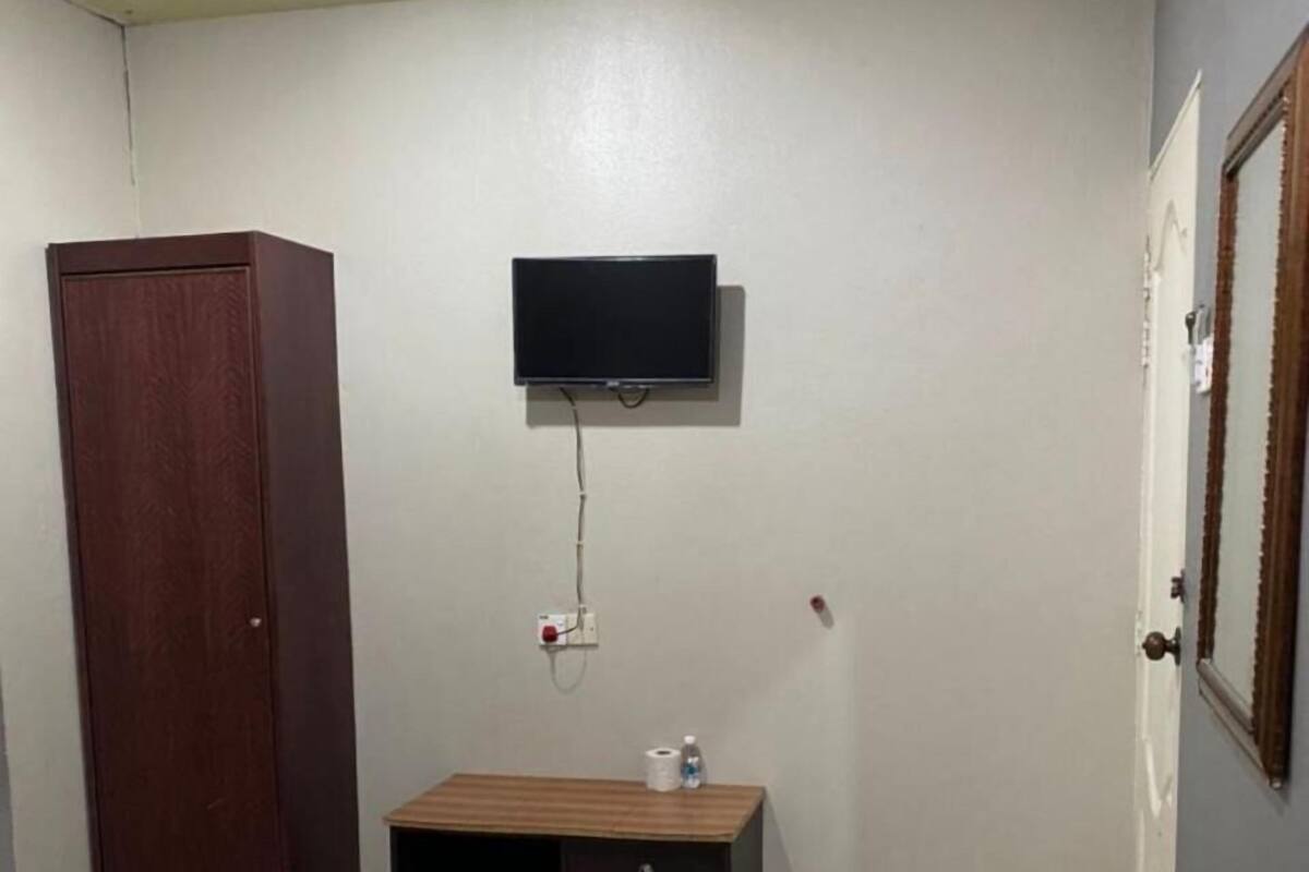 Un dormitorio con cama, un armario de madera, un mueble de madera pequeño, un televisor montado en la pared y una puerta con espejo.