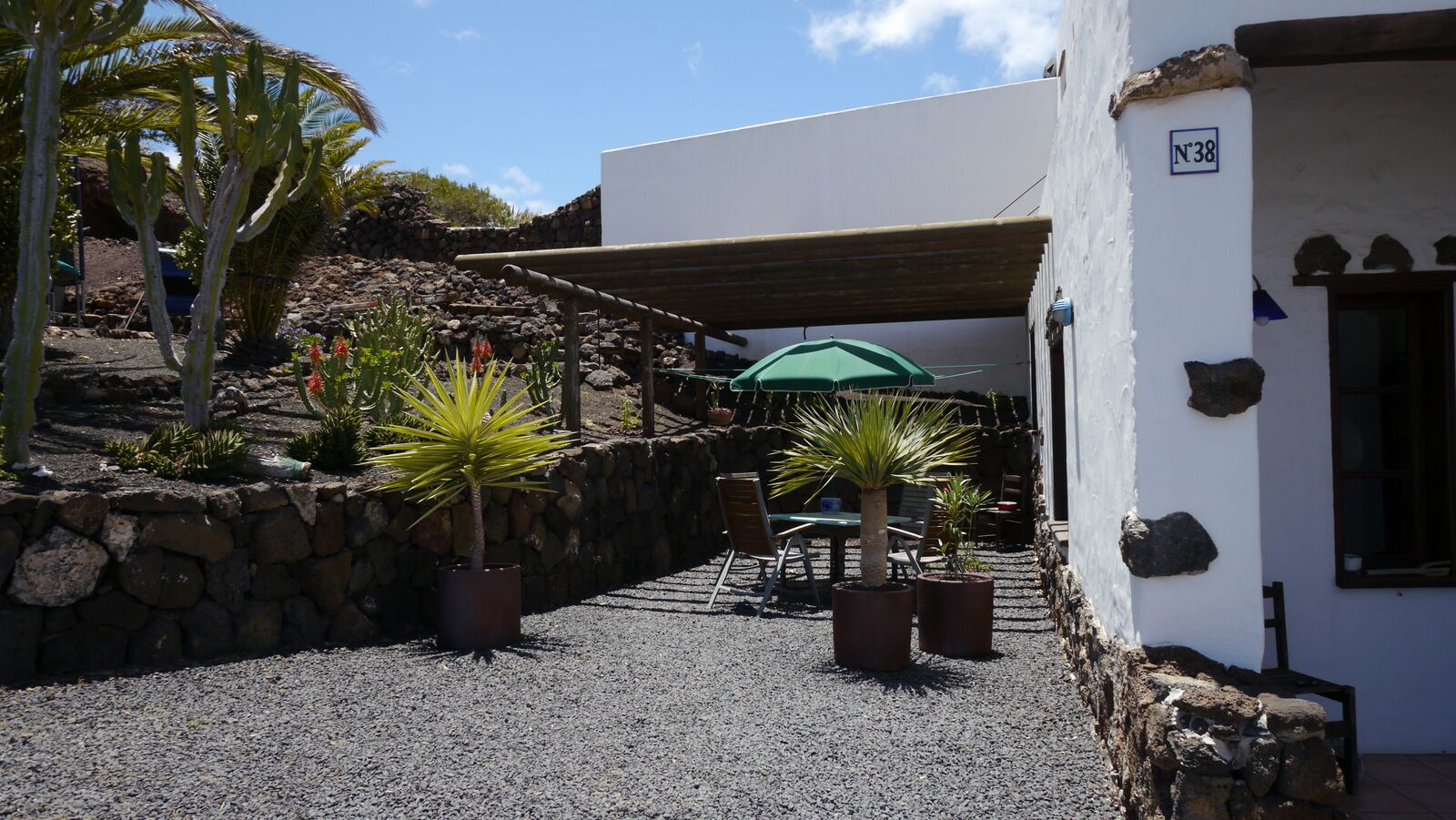 Un patio con muro de piedra, plantas en macetas, un área de estar cubierta y un edificio con un letrero que indica 'N°38'.