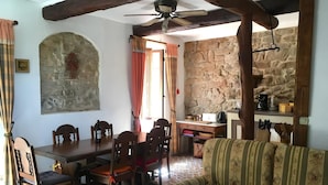 Un coin repas avec un mur en pierre, des meubles en bois et un ventilateur de plafond.
