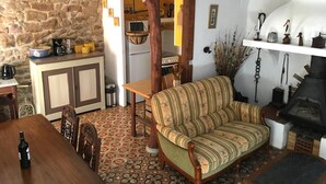 Un salon chaleureux avec un canapé en bois, une table à manger et un coin cuisine visible à travers une porte ouverte.