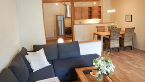A modern living room with a dark sofa, a coffee table, and a dining area with wicker chairs and a wooden table. - Ferienwohnung Krabbe (Kopendorf auf Fehmarn)