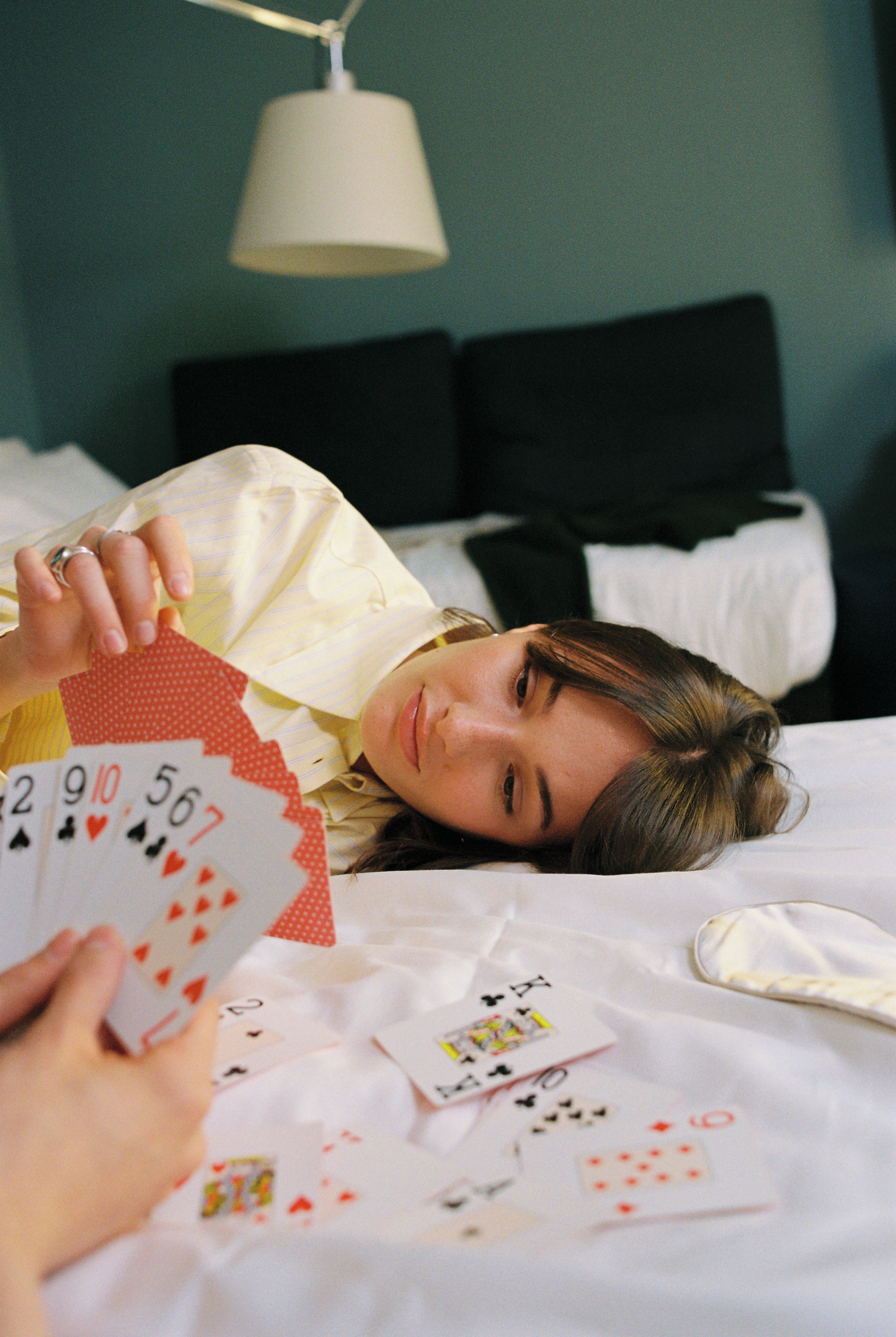 Uma pessoa deitada em uma cama com travesseiro branco e cobertor listrado, segurando cartas de baralho.