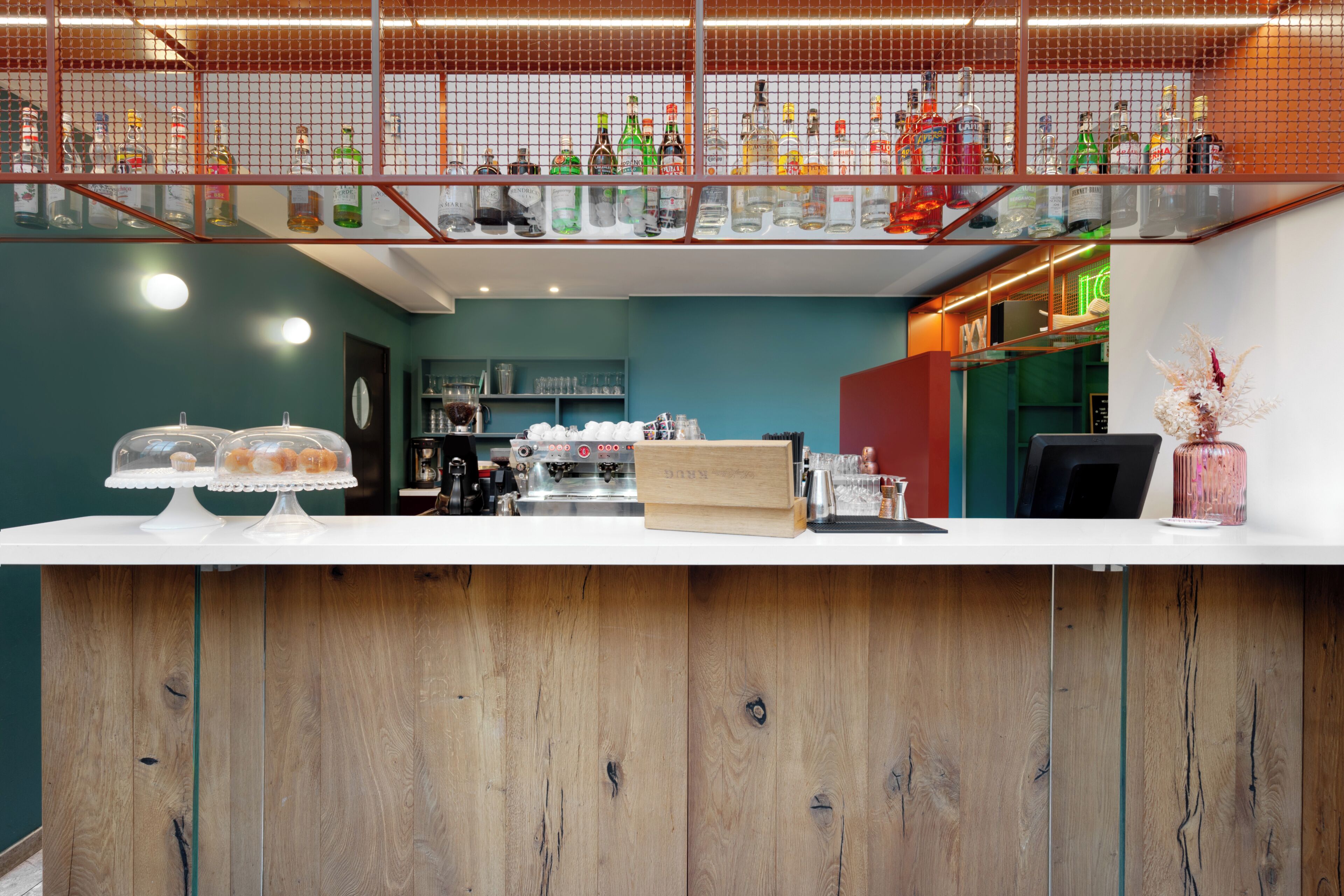 A bar area with a wooden counter, shelves with bottles, and a neon sign.