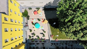 Vista aérea de un patio con mesas al aire libre, una piscina y un árbol grande.