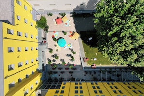 Vista aérea de un patio con mesas al aire libre, una piscina y un árbol grande.