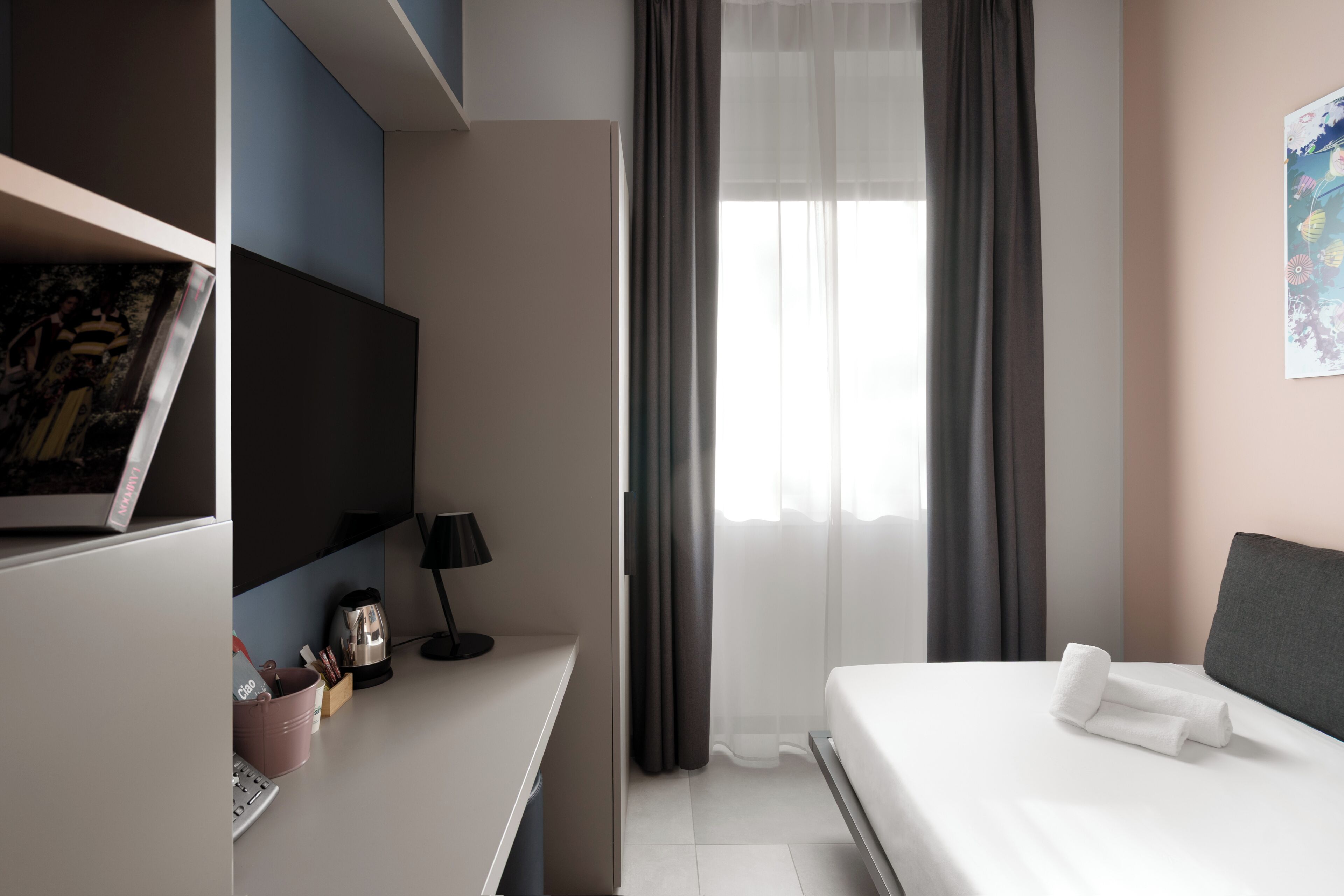 Ein modernes Hotelzimmer mit Bett, Schreibtisch, Fernseher und einem Fenster mit Vorhängen.