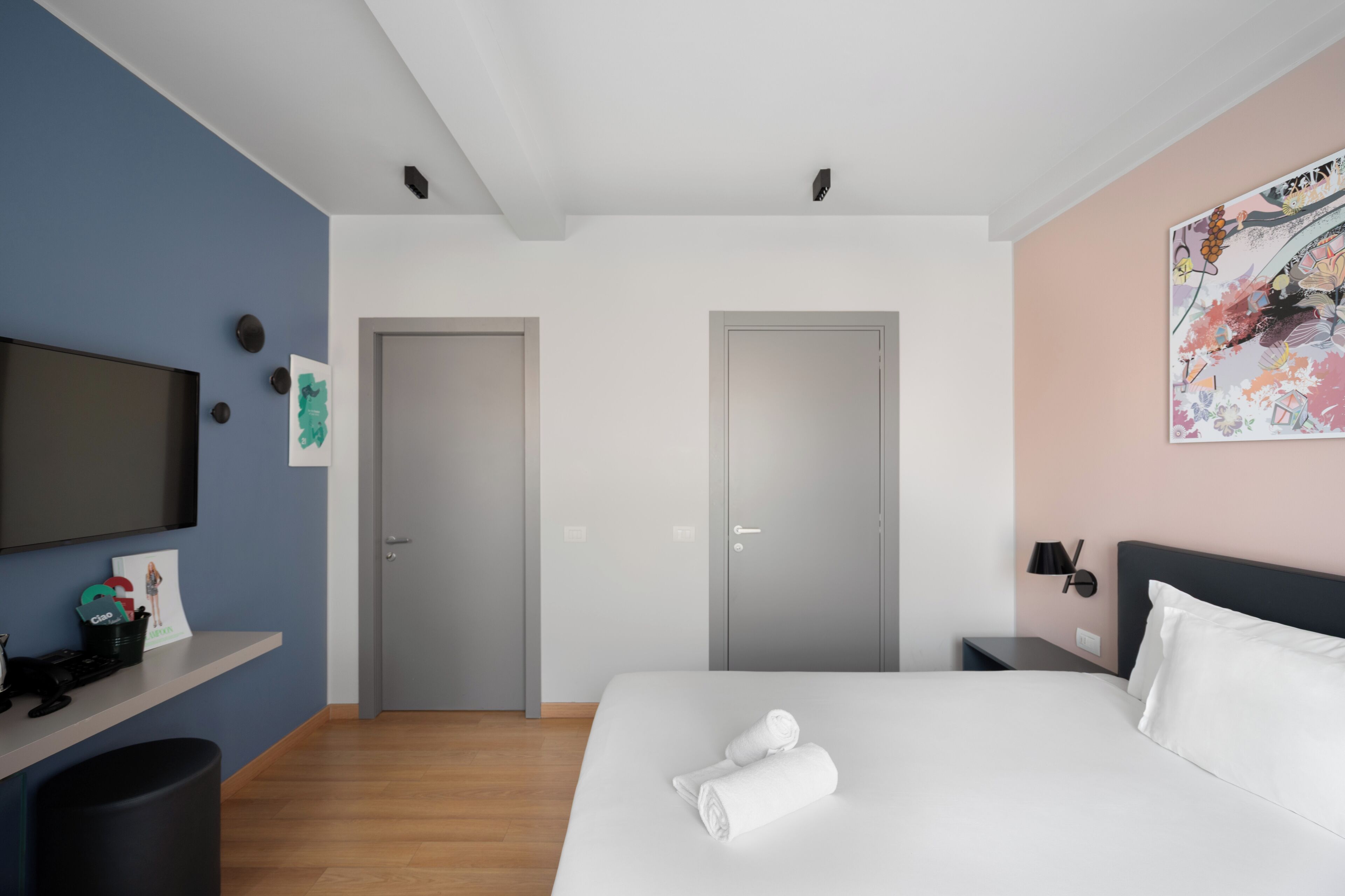 Una camera d'albergo moderna con un letto, una TV, una scrivania e un quadro appeso al muro.