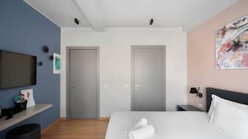 A modern hotel room with a bed, a TV, a desk, and a painting on the wall.