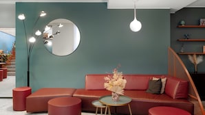 Un interior moderno con sofá rojo, una mesita redonda y un espejo grande sobre paredes color turquesa.