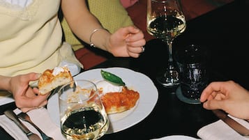 Ein Esstisch mit Speisen, Weingläsern und einer Person, die ein Pizzastück hält.