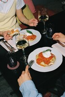 A dining table with plates of food, wine glasses, and a person holding a slice of pizza.