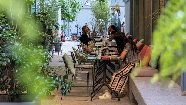 Un espacio exterior con mesas y sillas para comer, rodeado de follaje y plantas colgantes.