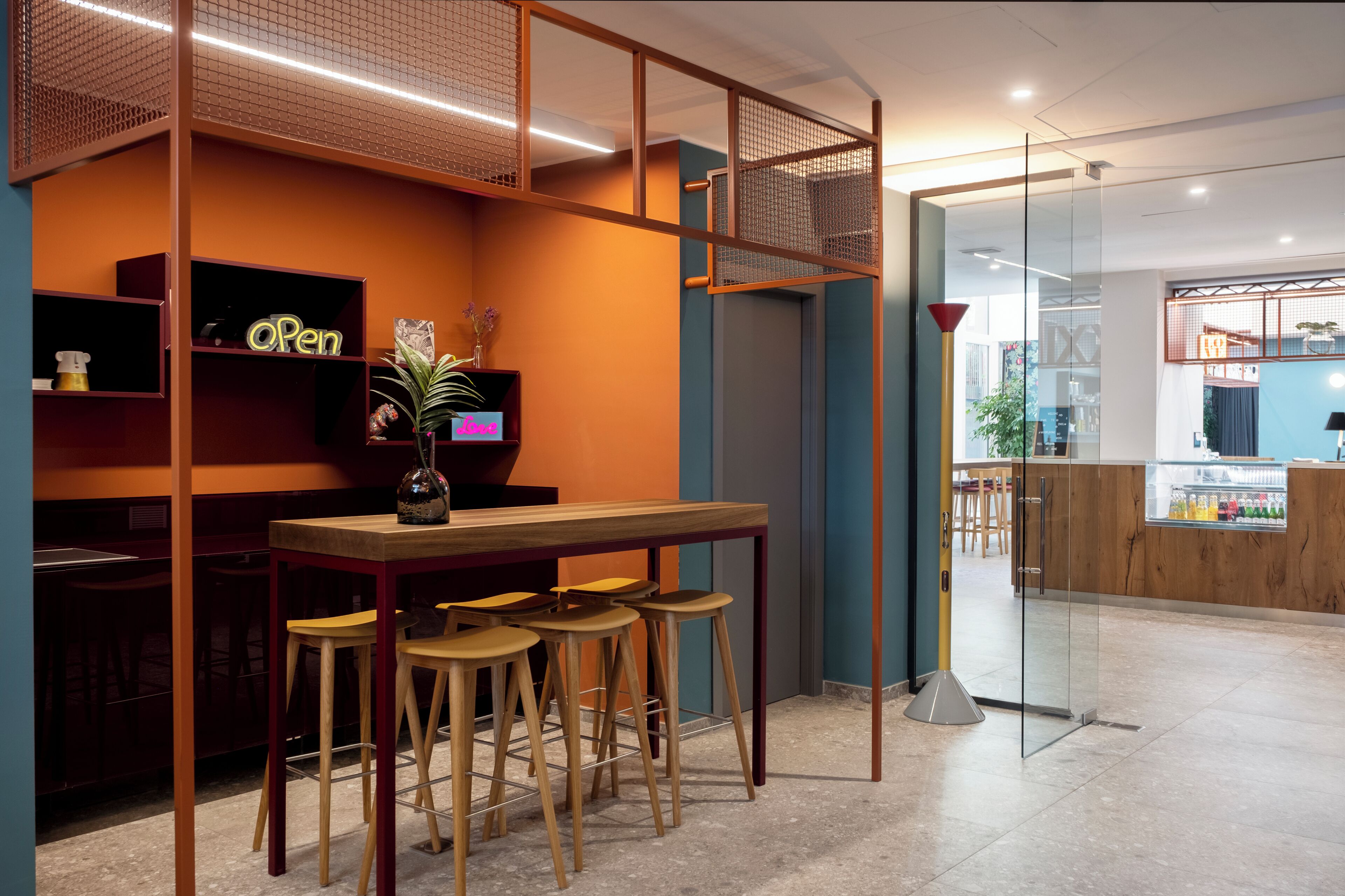 A bar area with stools, a wooden table, and a neon sign.
