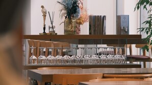 Interior de un restaurante con mesas y sillas de madera, y una exhibición de copas de vino.
