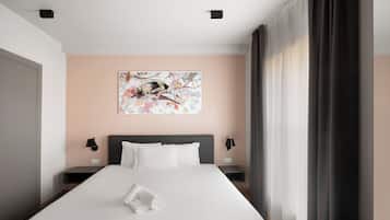 A hotel room with a bed, artwork on the wall, a nightstand, and a window with curtains.