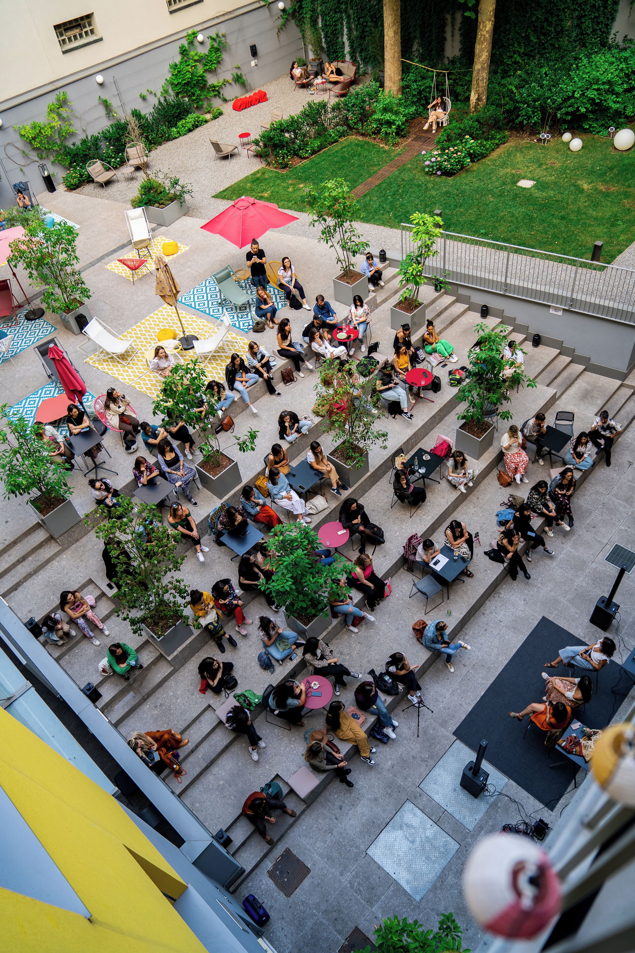 An outdoor seating area with tables and chairs, surrounded by greenery and potted plants.