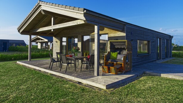 Een modern huis met een overdekte patio, terrasmeubels buiten en een verzorgd gazon.