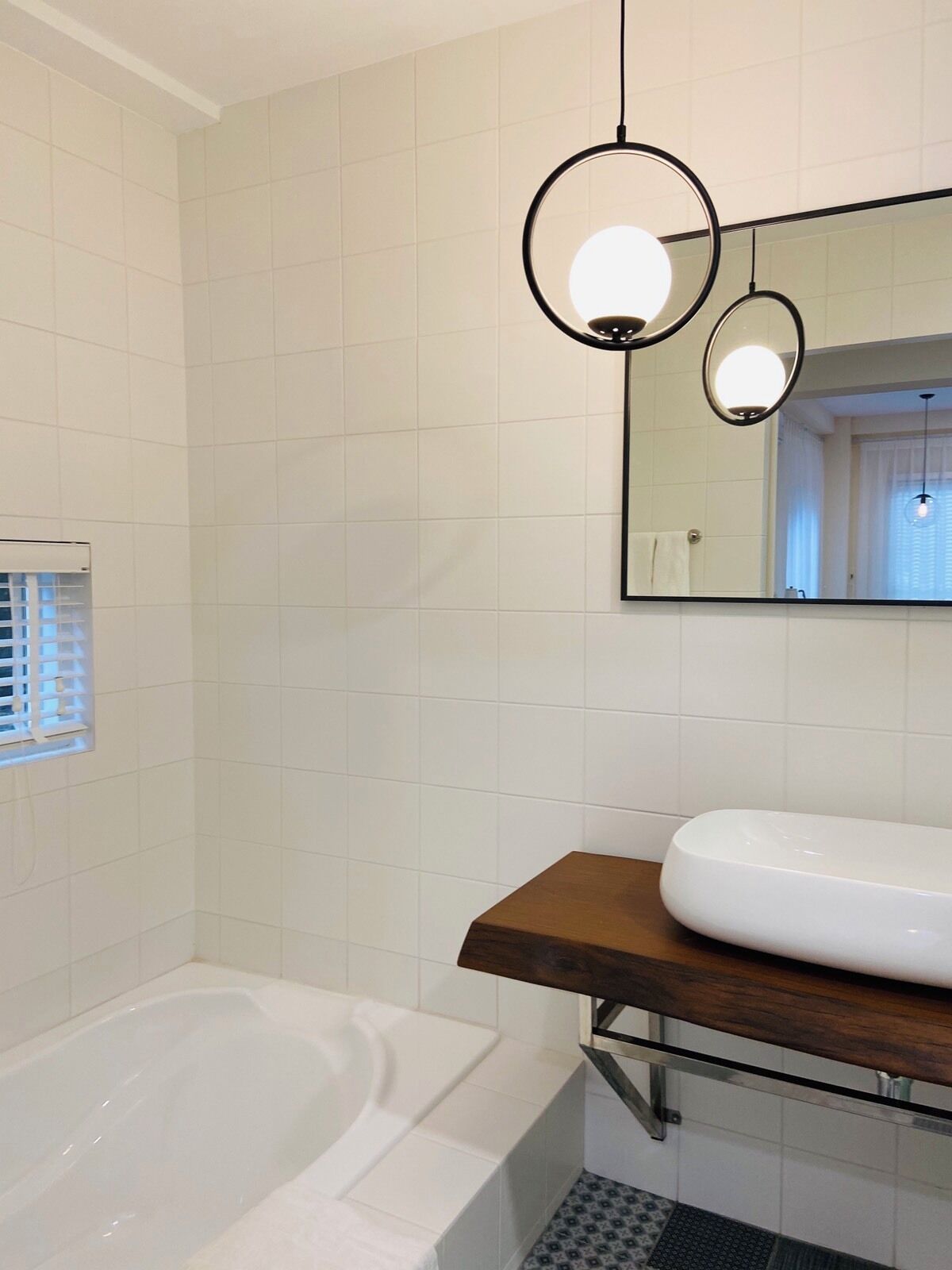 Ein modernes Badezimmer mit einer weißen Badewanne, einem Holzwaschtisch und einem großen Spiegel.