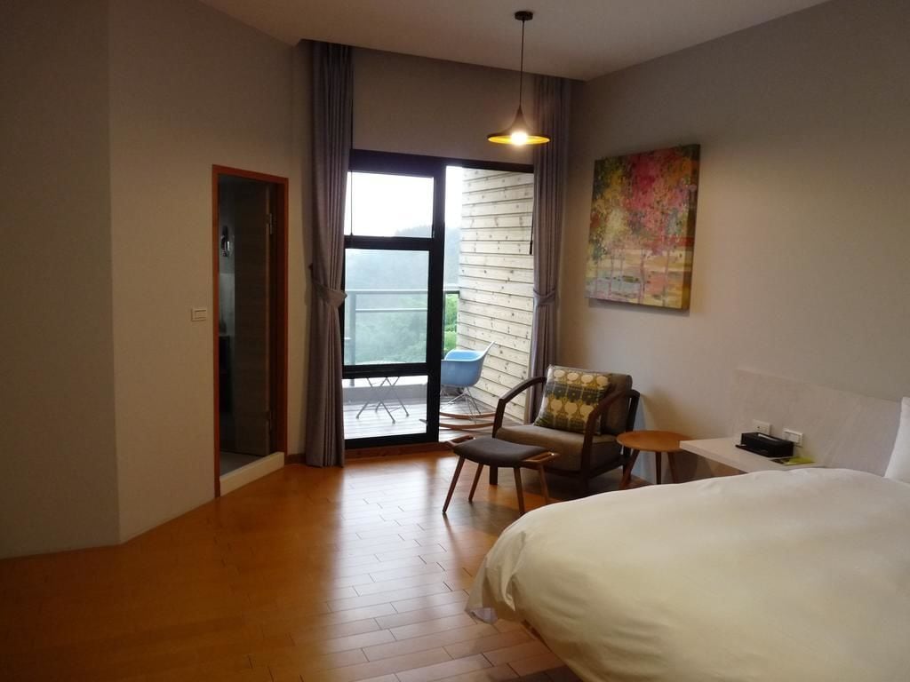 Une chambre d’hôtel avec un grand lit, une chaise, une petite table et une vue sur l’extérieur grâce à une porte vitrée.
