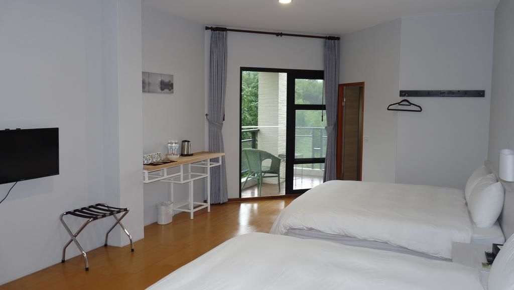 A hotel room with two beds, a TV, a small table with a kettle, and a balcony with a chair.