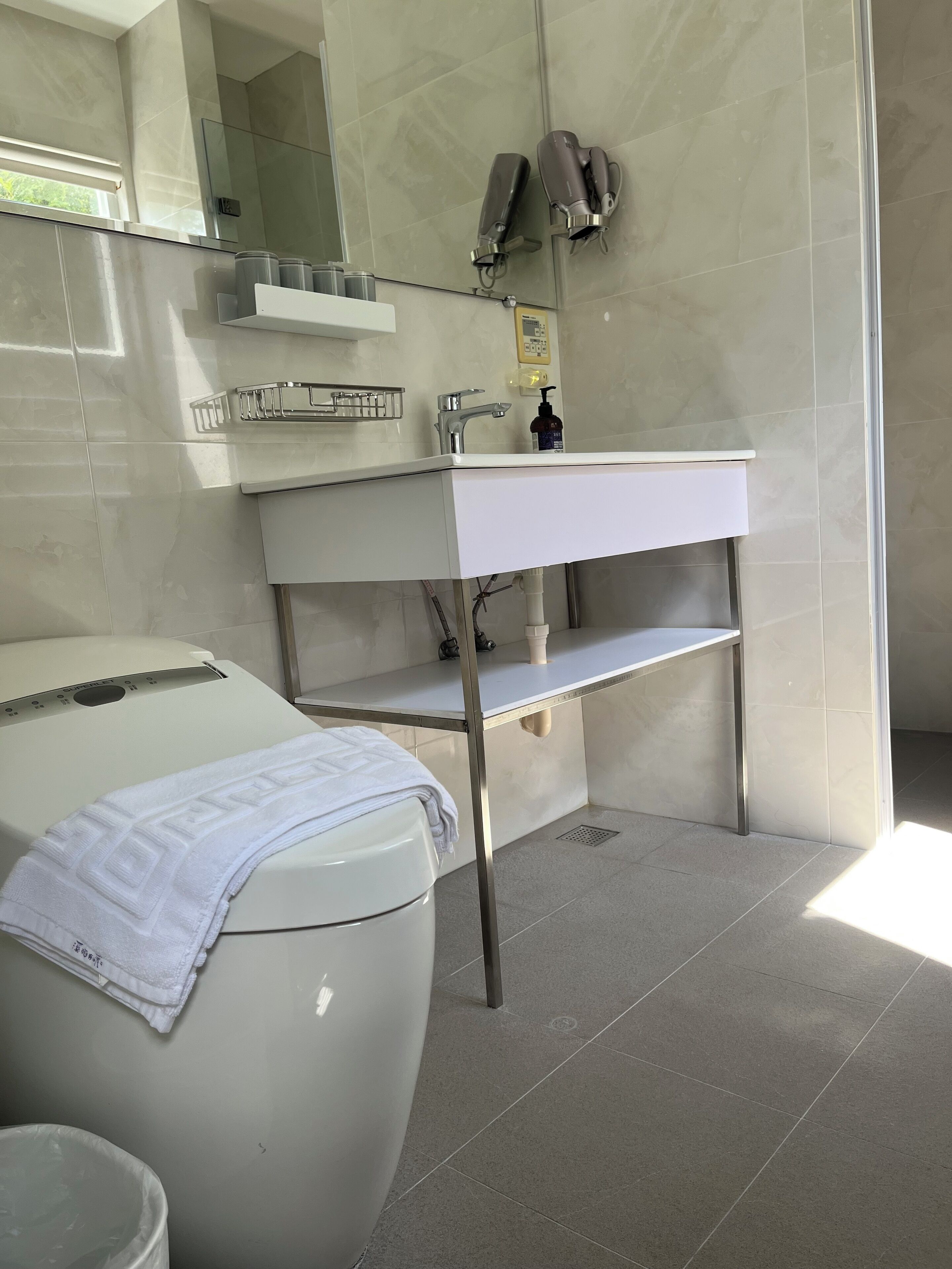 A modern bathroom with a white toilet, a white sink with a mirror above, and a towel on the toilet.