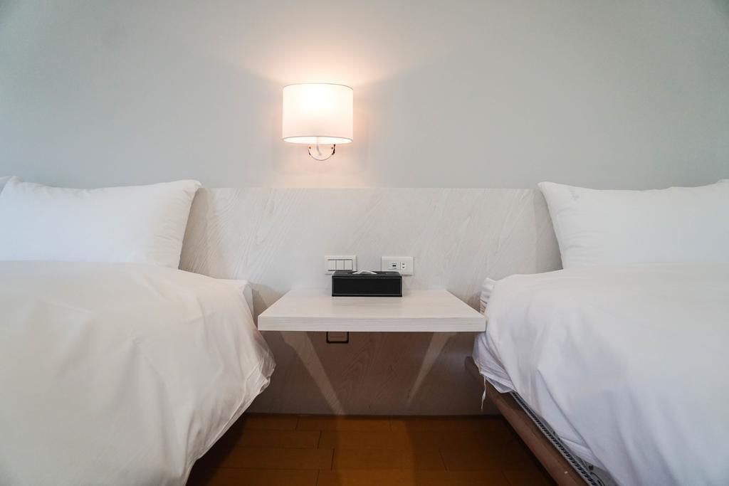 A hotel room with two single beds, a small bedside table with a lamp, and a power outlet.