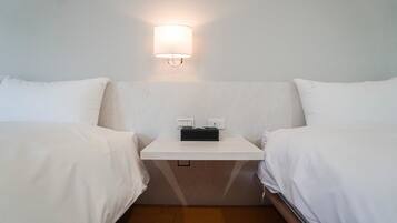 A hotel room with two single beds, a small bedside table with a lamp, and a power outlet.