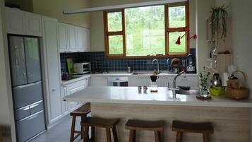 A modern kitchen with white cabinets, a large island with stools, a microwave, and a window overlooking greenery.