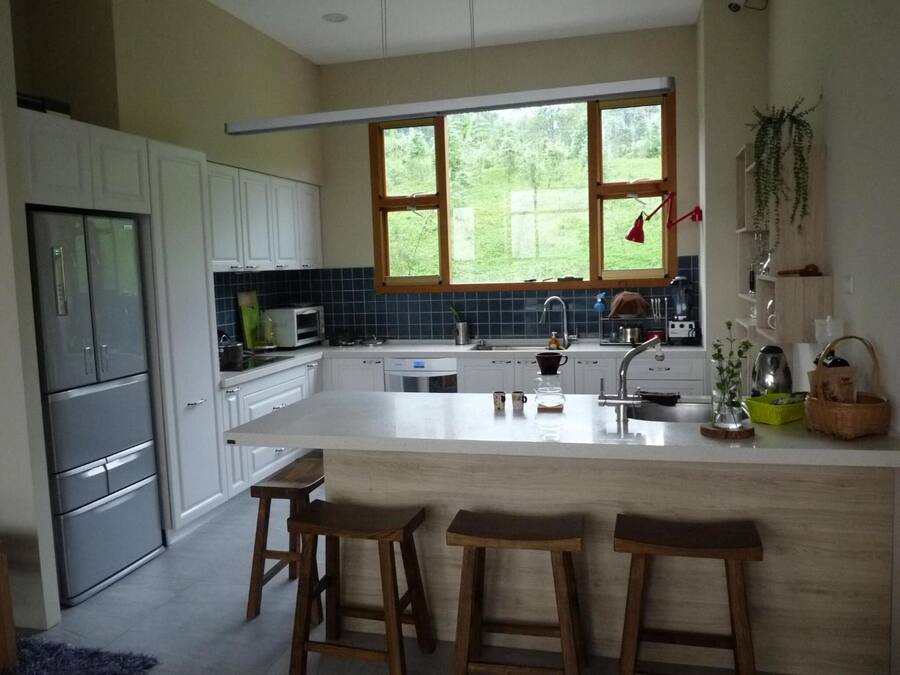 A modern kitchen with white cabinets, a large island with stools, a microwave, and a window overlooking greenery.